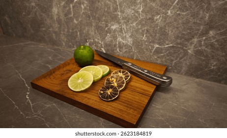 La Imagen muestra una tabla de cortar de madera con limas y un cuchillo. Hay una lima entera, tres rodajas de lima fresca y cuatro rodajas de lima seca. Un cuchillo de cocina con un mango de metal.