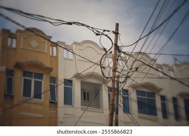 The image shows a wooden utility pole tangled with numerous overhead cables in front of a row of buildings with classic architectural designs, featuring arched windows and ornate facades - Powered by Shutterstock