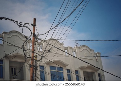 The image shows a wooden utility pole tangled with numerous overhead cables in front of a row of buildings with classic architectural designs, featuring arched windows and ornate facades - Powered by Shutterstock