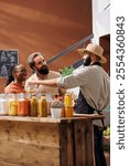 Image shows young multiethnic couple receiving assistance from middle eastern male vendor. Salesman wearing a hat and apron while speaking with customers in eco friendly convenience store.