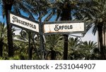 An image with a signpost pointing in two different directions in German. One direction points to success, the other points to failure.