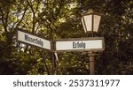 An image with a signpost pointing in two different directions in German. One direction points to success, the other points to failure.