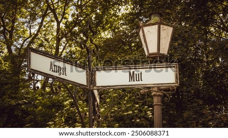 An image with a signpost pointing in two different directions in German. One direction points to courage, the other points to fear.