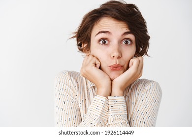 Image Of Silly Young Woman Pucker Lips And Lean Face On Hands, Listening With Interest, Looking At Camera, Standing Over White Background.