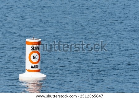 An image of a single red and white warning buoy near a designated lake side swimming area. 