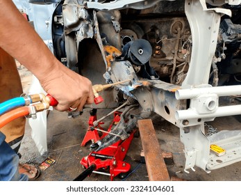 In the image, a skilled technician is diligently repairing a damaged car using a blowtorch. Sparks dance around as the technician precisely applies heat to reshape and fix the car's body, showcasing e - Powered by Shutterstock