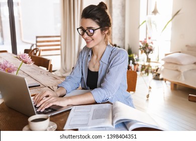 Изображение умной позитивной женщины 20 лет в повседневной одежде, печатающей на ноутбуке во время работы или учебы дома