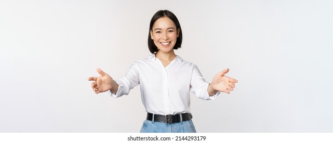 Image of smiling asian woman welcoming guests clients, businesswoman stretching out open hands, greeting, standing over white background