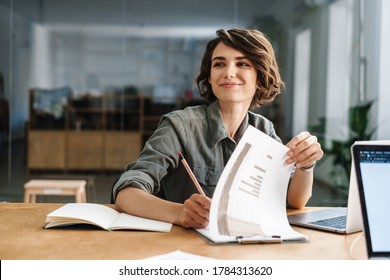 Image Of Smiling Beautiful Woman Writing Down Notes While Sitting At Table In Office