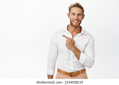 Image of smiling blond male model pointing finger left, showing logo promo aside, wearing white shirt and pants, studio background