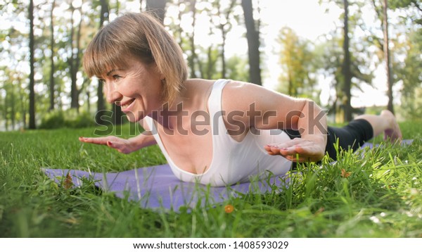 Image of smiling\
happy woman 40 years old doing yoga exercises on fitness mat at\
forest. Harmony of human in nature. Middle aged people taking car\
of mental and physical\
health