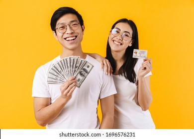 Image of smiling multinational couple showing dollars and credit card isolated over yellow background - Shutterstock ID 1696576231