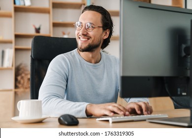 Image of smiling unshaven programmer man wearing eyeglasses working with computer in office