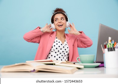 Image Of Smiling Woman Listening Music With Headphones While Working At Desk Isolated Over Blue Background