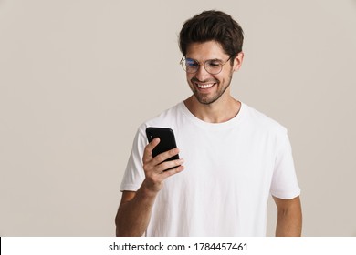 Image of smiling young man in eyeglasses using mobile phone isolated by white background