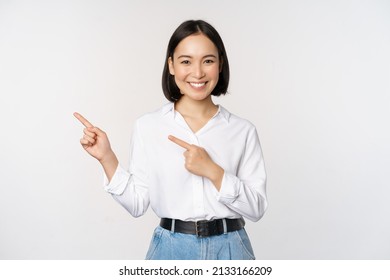 Image of smiling young office lady, asian business entrepreneur pointing fingers left, showing client info, chart of banner aside on copy space, white background - Shutterstock ID 2133166209