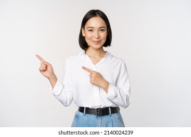 Image of smiling young office lady, asian business entrepreneur pointing fingers left, showing client info, chart of banner aside on copy space, white background - Shutterstock ID 2140024239