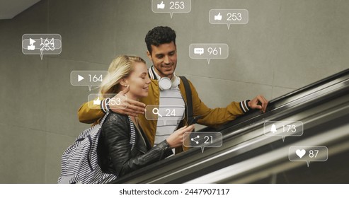 Image of social media icons floating over happy diverse couple embracing on moving stairs. social media and communication interface concept digitally generated image. - Powered by Shutterstock