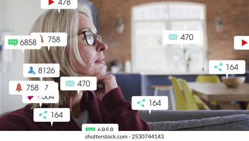 Image of social media icons and numbers over caucasian woman at home. Global social media, data processing and digital interface concept digitally generated image. - Powered by Shutterstock