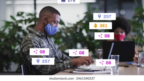 Image of social media icons over biracial man wearing face mask using laptop at office. Social media networking and covid-19 pandemic concept - Powered by Shutterstock