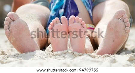 image of soles of two people sitting on sandy beach