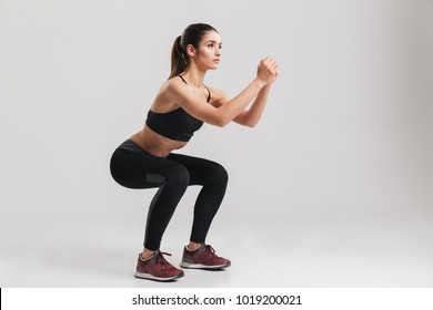 Image of sporty athletic woman in sneakers and tracksuit squatting doing sit-ups in gym isolated over gray background