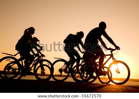 Image of sporty company  friends on bicycles outdoors against sunset. Silhouette