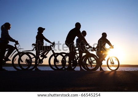 Image of sporty company friends on bicycles outdoors against sunset. Silhouette.