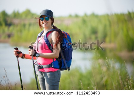 Image of sporty woman with walking sticks on background of lake and green vegetation