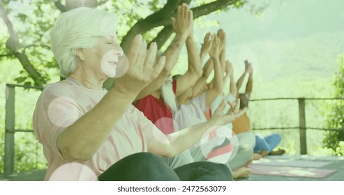 Image of spots of light and trees over diverse senior people practicing yoga in garden. Yoga, senior lifestyle, fitness, active lifestyle and retirement concept digitally generated image. - Powered by Shutterstock