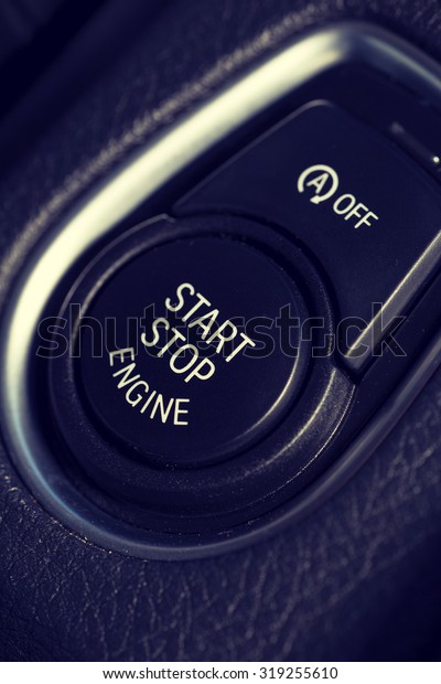 An image of a start\
and stop button in a modern car. Also a smaller button for\
switching the automatic feature off is above the button. Image has\
a vintage effect applied.