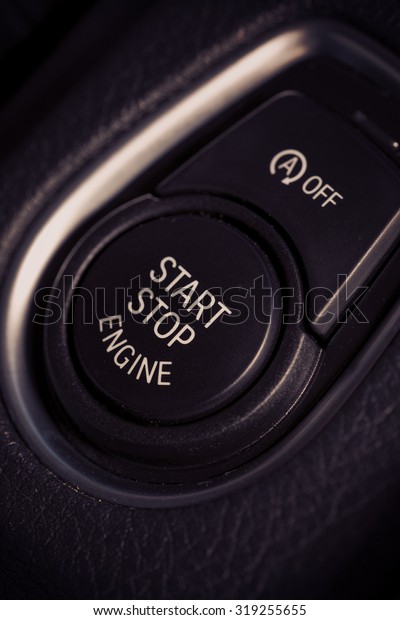 An image of a start\
and stop button in a modern car. Also a smaller button for\
switching the automatic feature off is above the button. Image has\
a vintage effect applied.