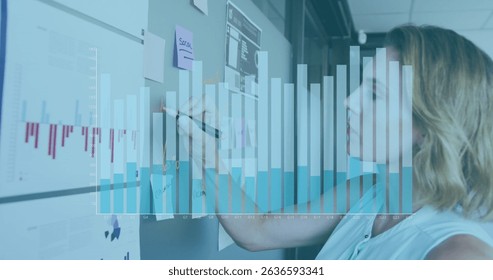 Image of statistics over caucasian businesswoman in office. Global data processing, business, finance and statistics concept digitally generated image.