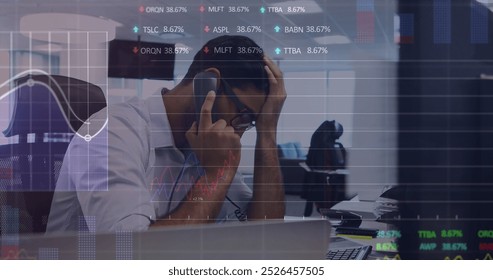 Image of stock market data processing over stressed biracial man talking on phone at office. Global economy and business technology concept