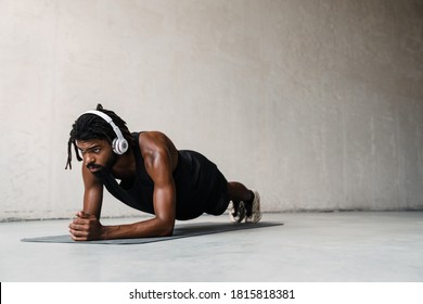 Image of strong african american sportsman in headphones doing exercise while working out on mat indoors