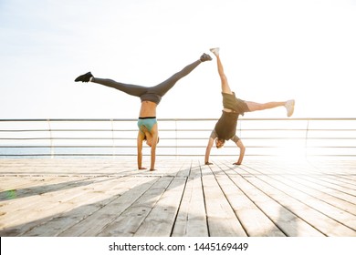 Image of strong two young sports woman and man friends loving couple at the beach near sea make cartwheel exercise. - Powered by Shutterstock