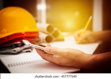 Image of structure engineer holding mobile smartphone calculate value in his product and drawing a building blueprint, hipster view vintage of photography.