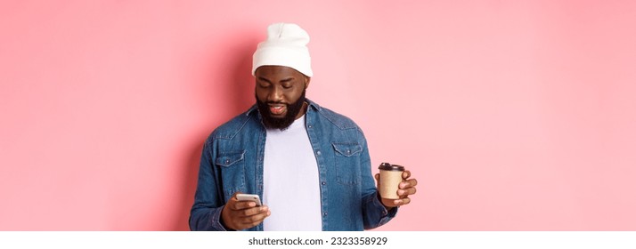 Image of stylish Black man hipster drinking takeaway coffee, reading message on phone, standing over pink background. - Powered by Shutterstock