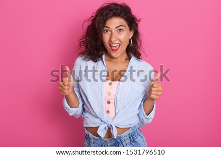 Image of success woman showing thumbs up, excited beautiful lady posing isolated over pink studio background, Caucasian model being in good mood, expresses positiv, keeps mouth opened. Human emotions.