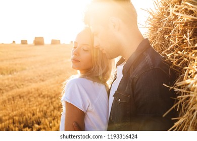 Image of sunlit couple man and woman walking on golden field after harvesting and standing near big haystack - Powered by Shutterstock