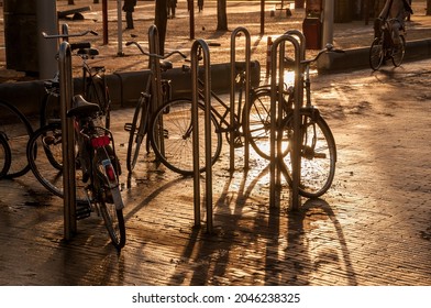 Image at sunset of several bicycles parked in a pedestrian zone of a city without cars. Clean air concept. The bikes cast their shadows on the wet ground. - Powered by Shutterstock