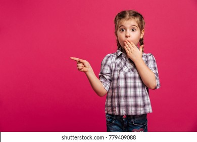 Image of surprised cute little girl child standing isolated over pink background. Looking camera pointing.