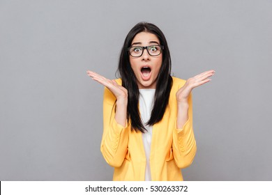 Image Of Surprised Woman Wearing Glasses And Dressed In Yellow Jacket Over Grey Background. Look At Camera.