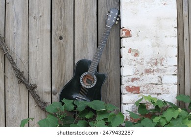 An image that captures a guitar sitting on the curb of an old barn made of brick and planks and a vine hanging from the wall. - Powered by Shutterstock