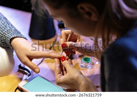 In the image there are two individuals engaged in a nail polish application activity