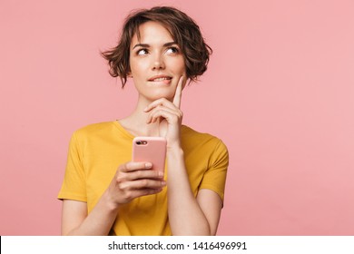 Image Of A Thinking Dreaming Young Beautiful Woman Posing Isolated Over Pink Wall Background Using Mobile Phone.