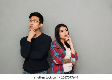 Image Of Thinking Serious Young Asian Loving Couple Standing Isolated Over Grey Wall Background Looking Aside.