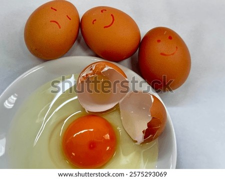 In the image, three brown eggs with smiley faces are drawn on them, placed above a white plate holding a cracked egg. The contents of the cracked egg—yolk and egg white—are visible on the plate alongs