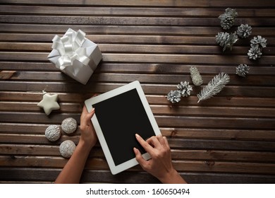 Image of three spice-cakes, decorative silver cones, giftbox and white toy star surrounding female hands touching display of digital tablet