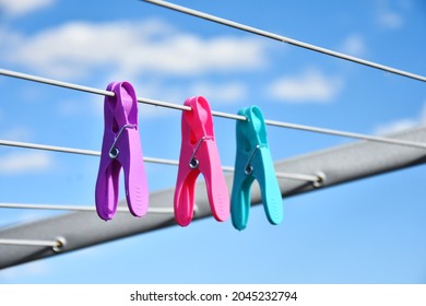 An image of three very colorful cloths pins on a clothesline. 